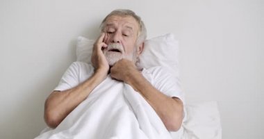 Yaşlı asyalı adam klinikte yatakta yatarken baş ağrısı hissediyor