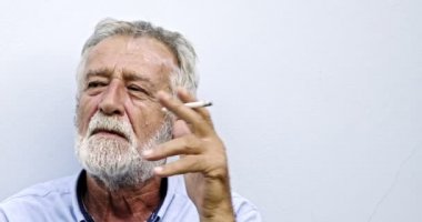 Yaşlı Asyalı adam beyaz arka planda sigara içiyor