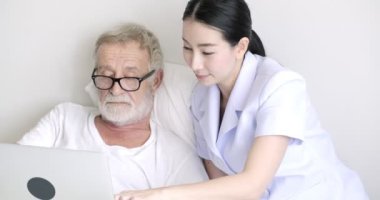 Genç asyalı hemşire ve olgun hasta dizüstü bilgisayarda bir şey izliyor