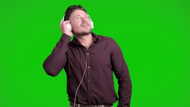 白种人正在耳机里听音乐 在绿色背景上跳舞 — 图库视频影像
