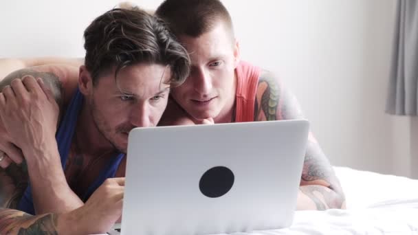 白人のゲイのカップルはベッドに横たわって 自宅でラップトップ上で何かを見ています — ストック動画
