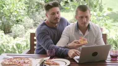 Kafkas eşcinsel çift akşam yemeği ve bahçede dizüstü bilgisayar kullanarak 