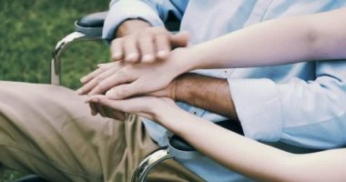 Tekerlekli sandalyedeki genç hemşire ve olgun engelli adam bahçede el ele tutuşuyor