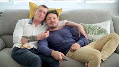 Kafkas eşcinsel çift evde kanepede yatıyor, kurabiye yiyor ve Tv izliyor 