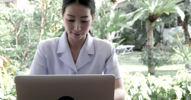 年轻的亚洲护士坐在花园里 使用笔记本电脑 — 图库视频影像