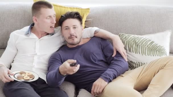 白人同性恋夫妇躺在家里的桌子上 吃饼干和看电视 — 图库视频影像