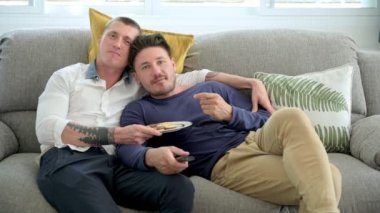 Kafkas eşcinsel çift evde kanepede yatıyor, kurabiye yiyor ve Tv izliyor  