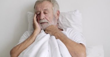 Yaşlı asyalı adam klinikte yatakta yatarken baş ağrısı hissediyor