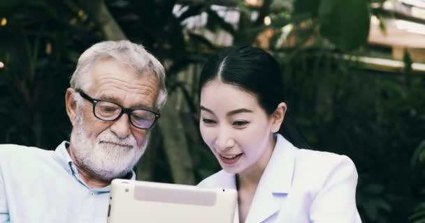 古いアジアの男性と若い看護師は 庭でタブレットPcを使用しています — ストック動画