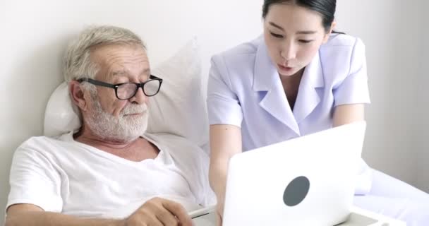 若いアジアの看護師と成熟した患者は ラップトップコンピュータ上で何かを見ています — ストック動画