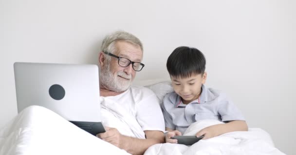 若いアジアの少年は クリニックでラップトップを使用して携帯電話と彼の祖父を使用しています — ストック動画