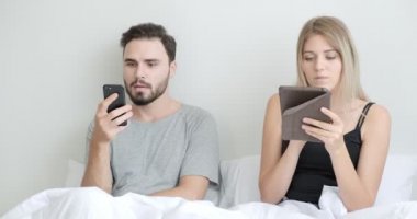 Çift yatakta cep telefonu ve tablet kullanıyor, ruh haline odaklanıyor. Beyaz erkek ve kadın..