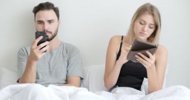 Çift yatakta cep telefonu ve tablet kullanıyor, ruh haline odaklanıyor. Beyaz erkek ve kadın..