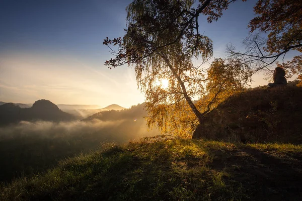 Meditation in epic sunrise light at the peak of an mesa in the german Saxon Switzerland National Park. Mountain range with light and fog. Hiking and climbing in wonderful mountain ranges of the Elbe Sandstone Mountains.