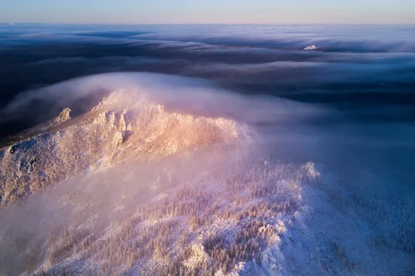 Aerial shot of Taganay mountains covered with clouds at sunny winter evening twilight