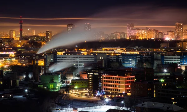 Telephoto lens long exposure shot of night cityscape with pipe and chimney emitting steam or smoke