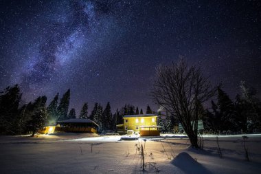 Rusya'da karanlık ormanda yalnız evin üzerinde renkli Samanyolu ile Gece manzara.