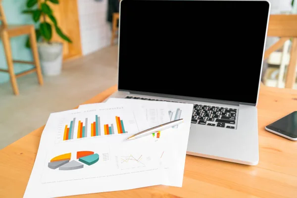 Laptop and business graph paper on wooden table — Stock Photo, Image