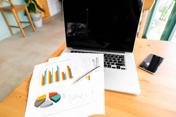 Laptop y papel gráfico de negocios en mesa de madera — Foto de Stock