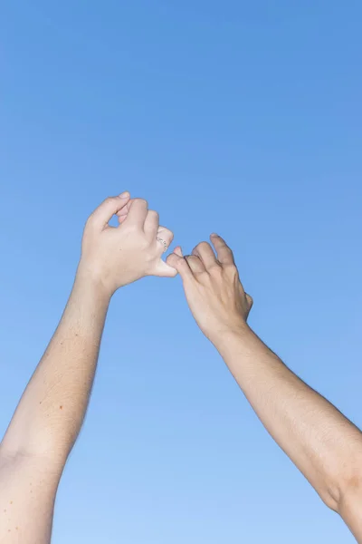 Closeup of young people holding hands over clear blue sky