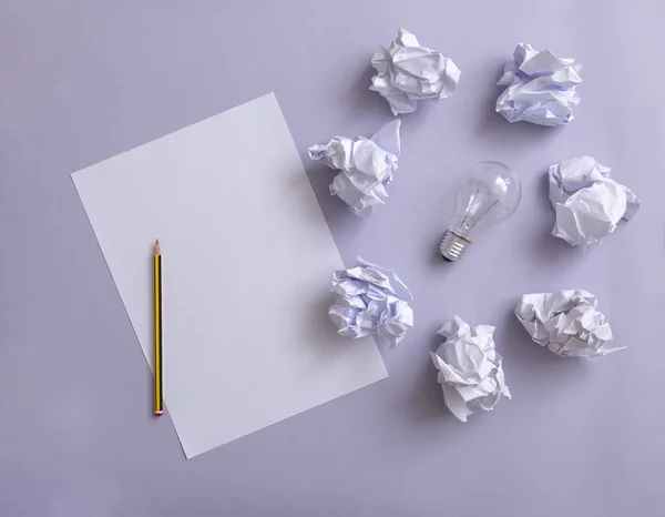 White paper with a pencil and wastepaper  surrounding a bulb on