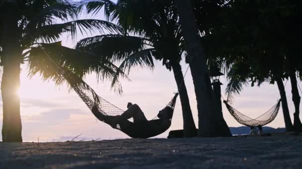 Een Man Liggend Een Hangmat Onder Palmbomen Tegen Achtergrond Van — Stockvideo