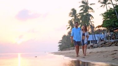 Genç, güzel bir kaç gün batımında bir kucaklama deniz kıyısı boyunca yürüyüş. Adam ve kız bir tropik adada balayına.