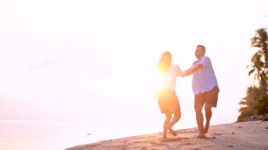 Genç, güzel bir kaç gün batımında bir kucaklama deniz kıyısı boyunca yürüyüş. Adam ve kız bir tropik adada balayına.