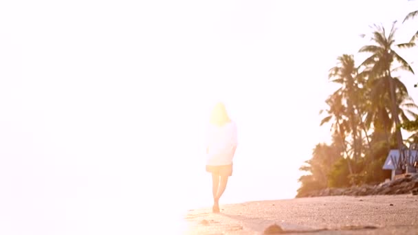在日落时 美丽的年轻女子沿着热带岛屿的海岸散步 愉快的女孩在沙滩上微笑 — 图库视频影像