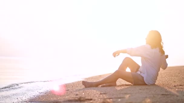 美しい女性は 砂浜に座っているし 距離に見えます 彼女のボーイ フレンドを待っている海のそばに座って幸せな女の子 — ストック動画