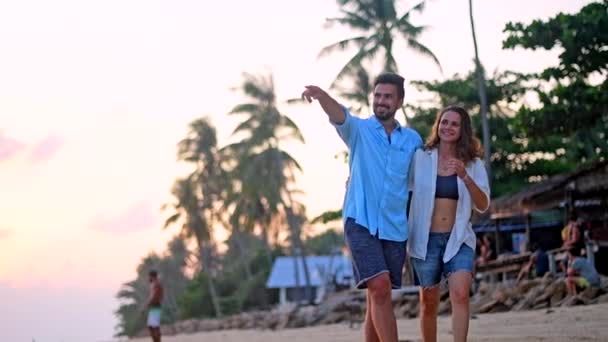 夕日海岸沿いを抱きしめることで歩く若い 美しいカップル 男と女の新婚旅行の熱帯の島に — ストック動画