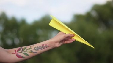 Elinde bir dövme ile Genç, güzel bir kız bir kağıt uçak başlattı. Güzel kadın, doğada açık havada, gün batımı, renkli bir kağıt uçağı başlattı.