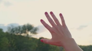 Bir kadın elin yakın çekim, Güneş parmaklar aracılığıyla parlayan. Güneş ışınları, gün batımında bir kızın parmaklarıyla parlıyor..