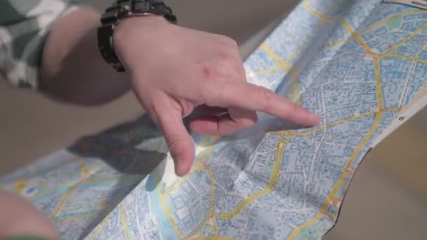 特写手在纸质地图上显示路线 在城市的户外 游客们为城市地图铺路 白皮肤的人用手指指着地图 一个男人和一个女人看着地图 讨论路 — 图库视频影像