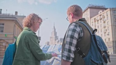 Turistler büyük bir şehirde durmak ve sahne keyfini çıkarın. Moskova'da sevgi dolu bir çift turist. İki kişi arkalarında duruyor. Arka planda yüksek katlı.