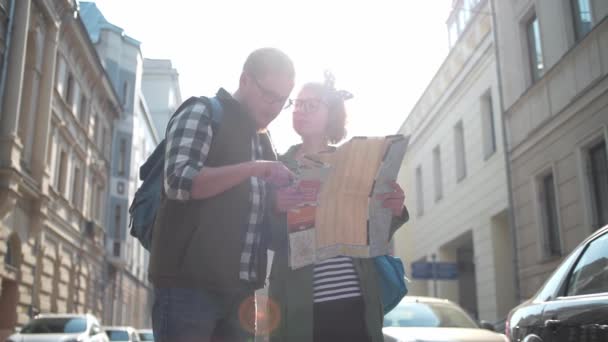 年轻漂亮的游客在夏天漫步在老城区 看看地图 游客在城市迷路了 路线选择 在纸质地图上搜索道路 一起旅行年轻的家庭一对可爱的游客周游世界 — 图库视频影像
