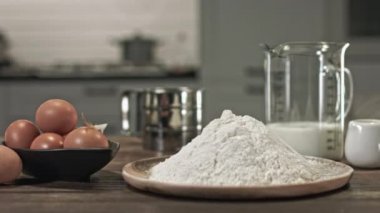 Evde güzel bir tatlı yapmak için gerekli malzemeler, ahşap bir masada uzanmak için. Sürgüde düzgün bir hareket var. Metal kase. Cam kase. Küçük tavuk tüyü.