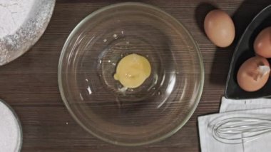 Tahta masadaki en iyi plan malzemeleri. Çiğ yumurtalar cam bir kasede kırıldı. Hamur işi pişirmek için. Pasta için dondurma yapıyorum. Mutfak ürünleri ile birlikte kameranın hareketi.