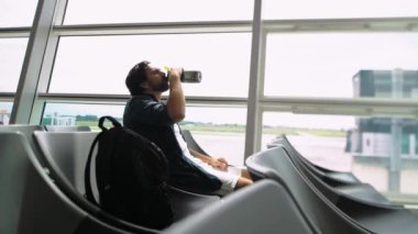 Bir adam havaalanı salonundaki şişeden su içiyor. Yakışıklı, çekici, melez bir genç adam uçağa binmeden önce havaalanında oturuyor. Turist su içer..