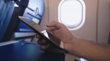 Çekici bir adam uçakta tek başına oturuyor ve elinde bir akıllı telefon tutuyor. Bir siteyi cep telefonuna kaydırmak. Sivil havacılıkta kablosuz teknolojiler. Uçakta kanepede bir turist oturuyor..