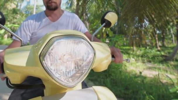 若い魅力的な男が黄色い自転車に腰を下ろしている 雨林の間の道路上でスクーターを起動します — ストック動画
