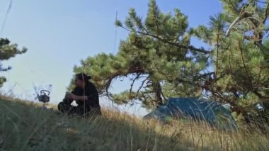 Kamp alanında genç ve yakışıklı bir adam gaz ocağını yakıyor. Kaynar su. Çadıra park etmek. Seyahat gaz ocağı. Bir turist fincandan çay içiyor.