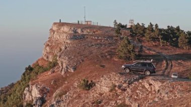 Bir dağın yamacında bir SUV duruyor. Araba denizin arka planında bir kayanın üzerinde duruyor. Arabayla seyahat et.