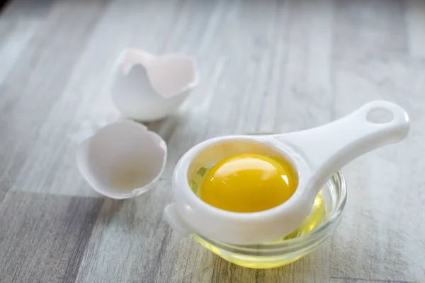 Ayıran yumurta beyazı ve sarısı ahşap masa ve kırık yumurta kabukları arka plan vardır