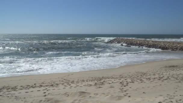 Vista de una hermosa playa de arena oceánica con las olas azules rodando en la orilla, algunas rocas presentes . — Vídeo de stock