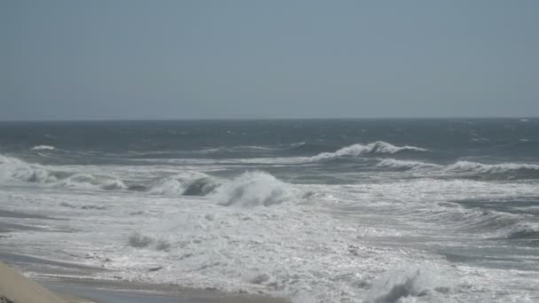 Vue sur une belle plage de sable de l'océan avec les vagues bleues se déversant dans le rivage, quelques rochers présents . — Video