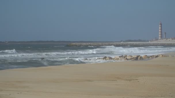 Vista de una hermosa playa de arena oceánica con las olas azules rodando en la orilla, algunas rocas presentes . — Vídeo de stock