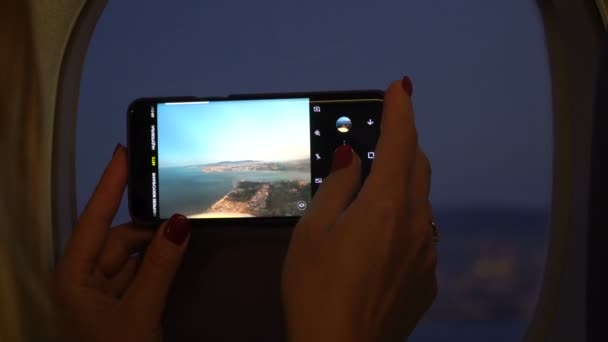 Крупним планом жінка рука тримає мобільний телефон і фотографується за вікном літака — стокове відео