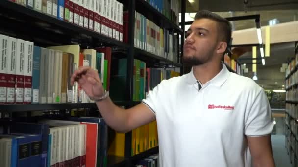 젊은 대학 학생 복용 책 도서관에 선반에서. 라이브러리에 잘생긴 젊은 남자. 마그데부르크, 독일입니다. 01.09.2018 — 비디오