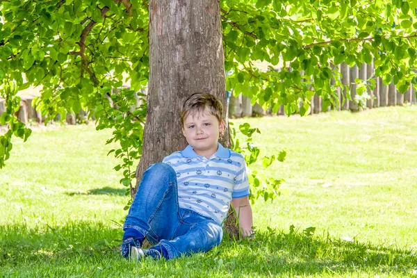 少年は木陰に木の下に座っている 太陽から隠れて — ストック写真